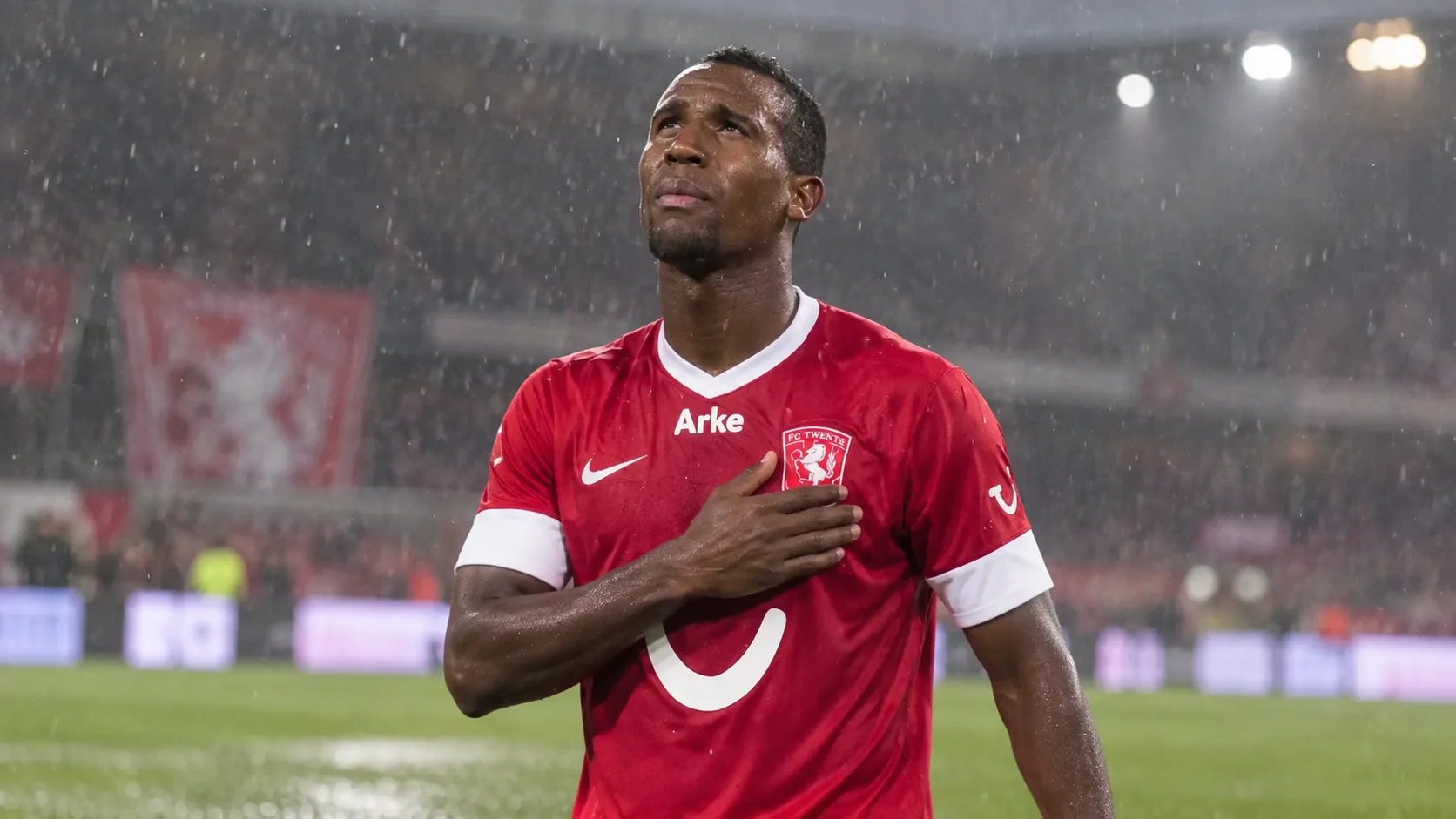 Douglas Teixeira in het rode tenue van FC Twente op een regenachtig voetbalveld.