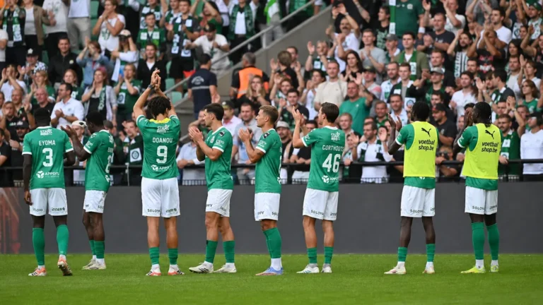 Een groep voetballers in groene shirts applaudisseert voor een volle tribune met supporters.