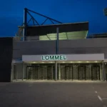 De lege ingang van het stadion in Lommel met een vast clubbord aan de gevel.