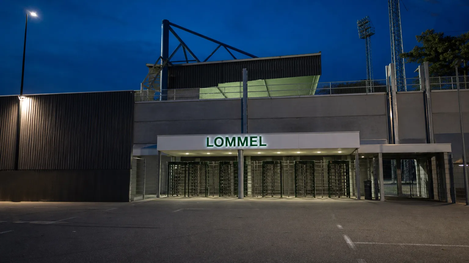De lege ingang van het stadion in Lommel met een vast clubbord aan de gevel.