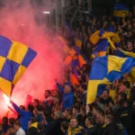 Supporters van SK Beveren met geel-blauwe vlaggen in de tribune.