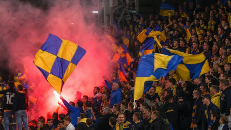 Supporters van SK Beveren met geel-blauwe vlaggen in de tribune.