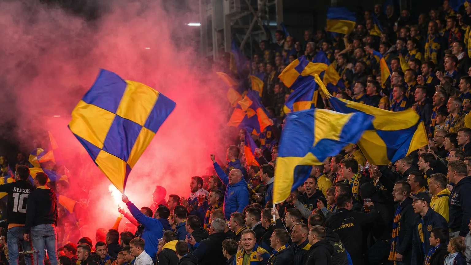 Supporters van SK Beveren met geel-blauwe vlaggen in de tribune.