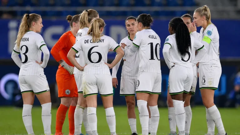 Speelsters in witte tenues vormen een hechte kring op het veld.