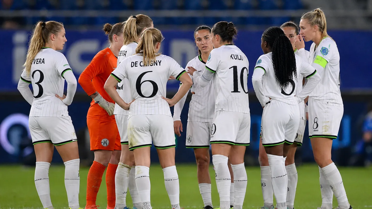 Speelsters in witte tenues vormen een hechte kring op het veld.