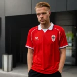 Arthur Vermeeren in een rood Antwerp-shirt aan een clubgebouw.