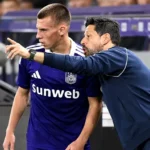 Een Anderlecht-trainer geeft aan de zijlijn aanwijzingen aan een speler in paars tenue.