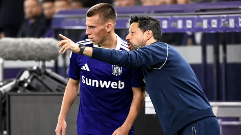 Een Anderlecht-trainer geeft aan de zijlijn aanwijzingen aan een speler in paars tenue.