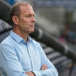 Jess Thorup kijkt geconcentreerd vanop de zijlijn in een stadion.