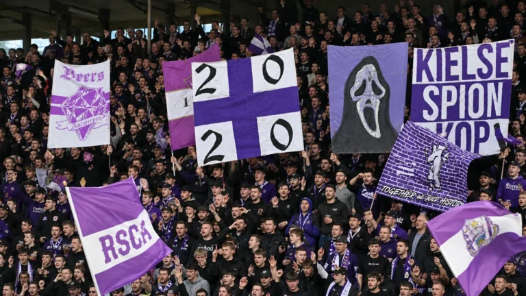 Een volle paars-witte voetbaltribune met supporters die grote spandoeken omhooghouden.