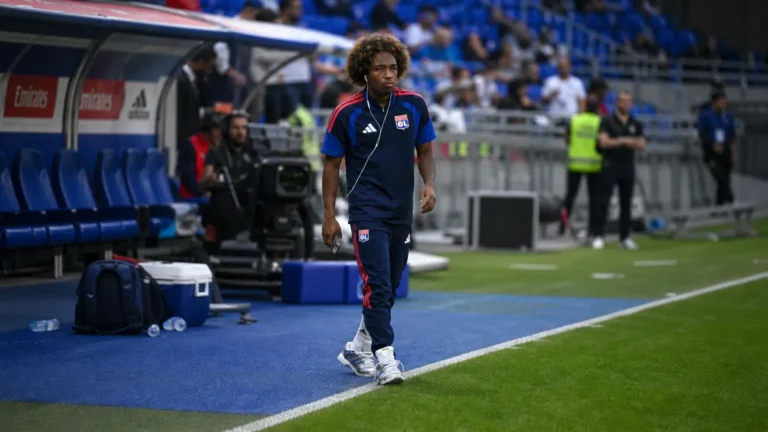 Malick Fofana in donkere trainingskleding langs de zijlijn van een voetbalveld.