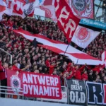 Een groep Antwerp-supporters met rood-witte vlaggen op de tribune.
