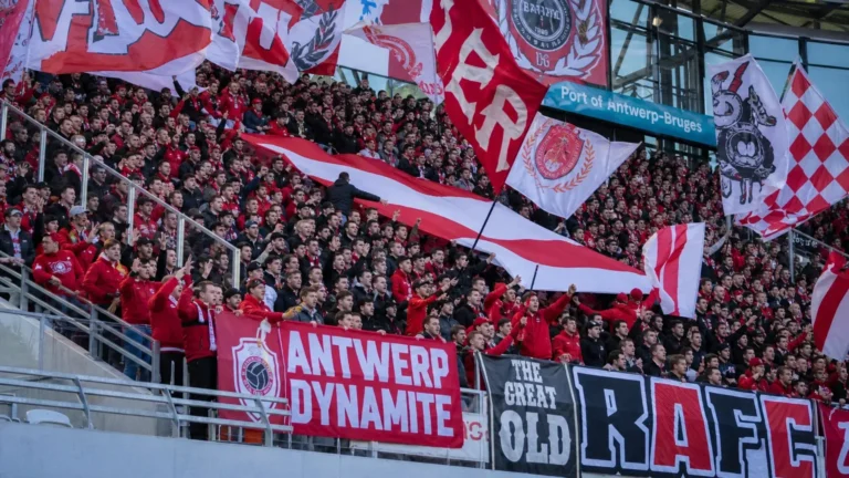 Een groep Antwerp-supporters met rood-witte vlaggen op de tribune.