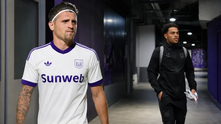 Twee voetballers wandelen door de overdekte ingang van een clubcomplex.