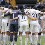 Club Brugge-spelers vormen een kring op het veld in hun witte wedstrijdtenues.