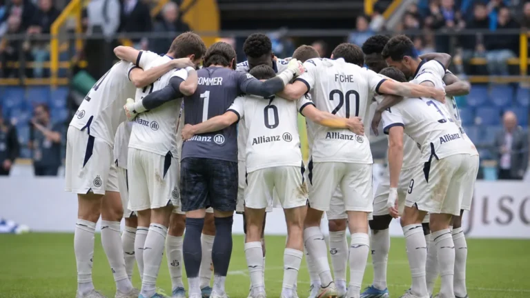 Club Brugge-spelers vormen een kring op het veld in hun witte wedstrijdtenues.