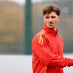 Thomas Meunier in een rode trainingsjas naast een oefenveld.