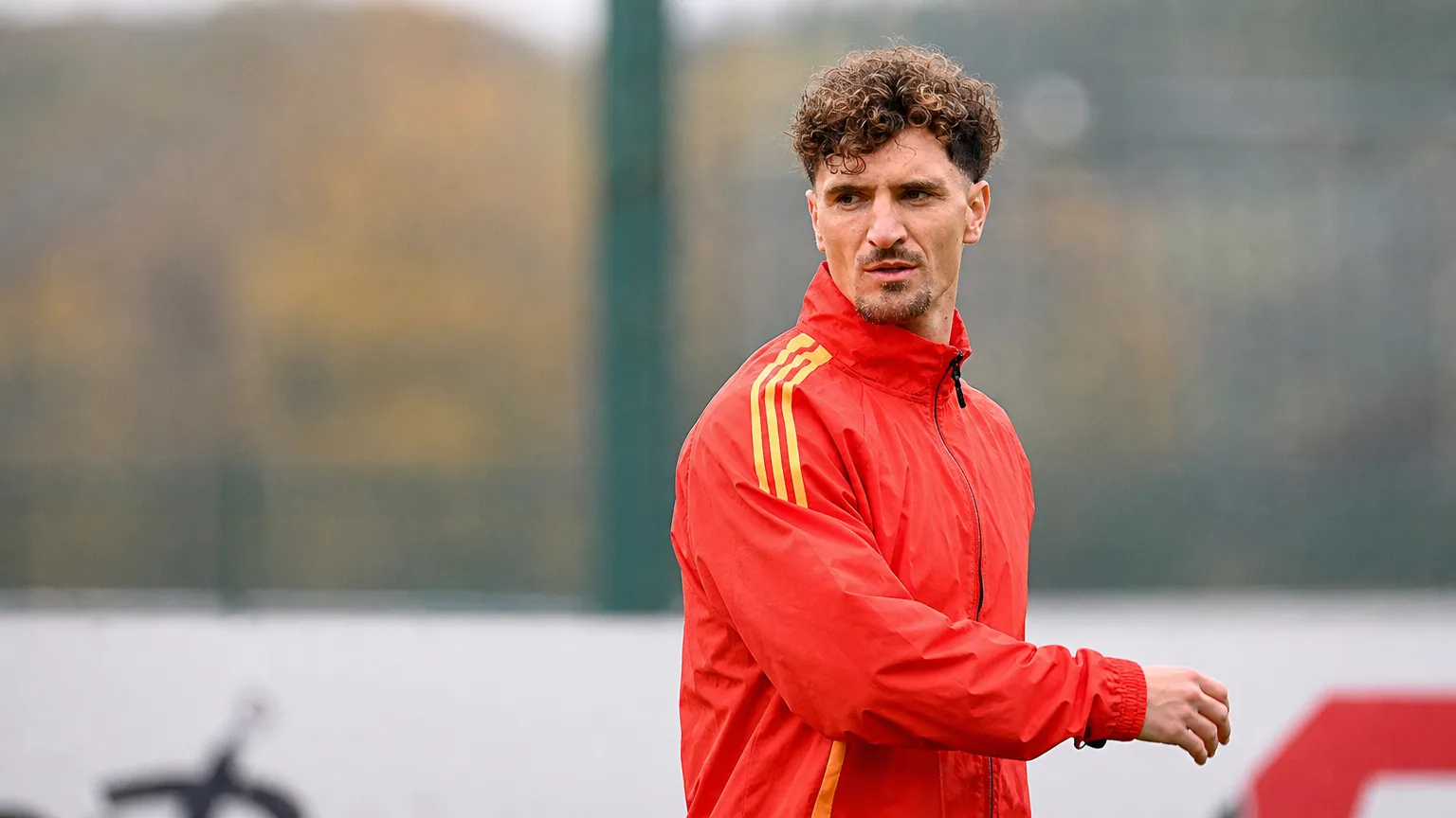 Thomas Meunier in een rode trainingsjas naast een oefenveld.
