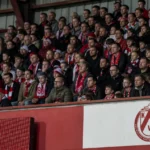 Een groep supporters van KV Kortrijk op de thuistribune, met een clubembleem op een tribune­bord.
