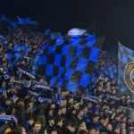 Supporters van Club Brugge zwaaien met blauw-zwarte vlaggen op de tribune.