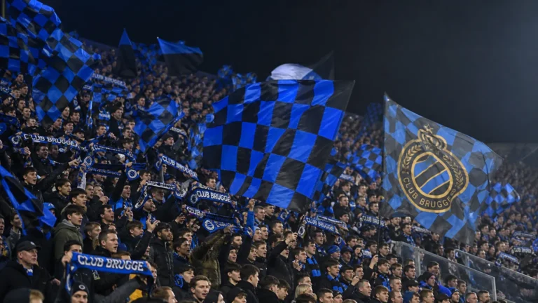 Supporters van Club Brugge zwaaien met blauw-zwarte vlaggen op de tribune.