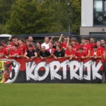 Kortrijkse supporters tonen een spandoek langs het trainingsveld.
