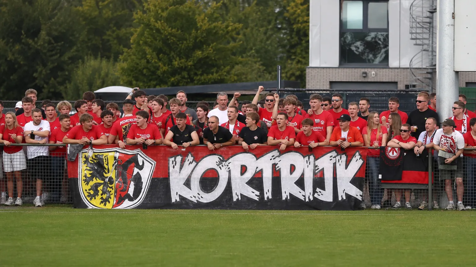 Kortrijkse supporters tonen een spandoek langs het trainingsveld.