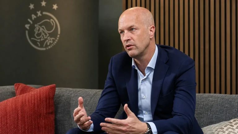 Jordi Cruijff spreekt in een Ajax-medialokaal met een Ajax-embleem op de wand.