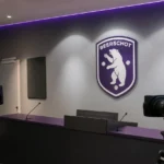 Lege mediaruimte van Beerschot met camera-apparatuur en een vast clubembleem aan de wand.