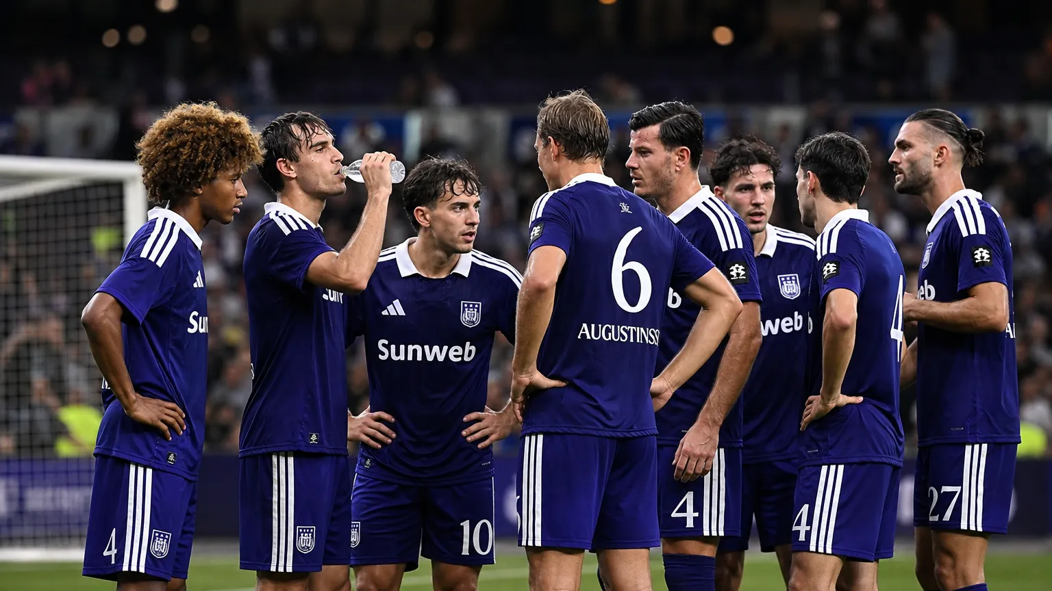 Een groep voetballers in paarse tenues overlegt op het veld na een wedstrijd.