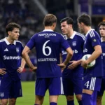 Een groep Anderlecht-spelers in paarse wedstrijdtenues verzamelt zich op het veld.