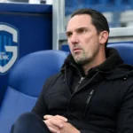 Dimitri De Condé zit in de Cegeka Arena met een KRC Genk-embleem op de vaste dug-outwand.