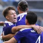 Drie Anderlecht-spelers vieren samen op het veld in paarse wedstrijdshirts.