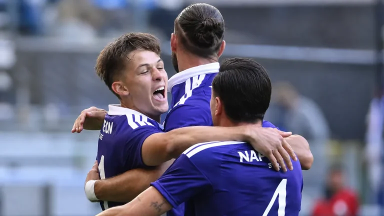 Drie Anderlecht-spelers vieren samen op het veld in paarse wedstrijdshirts.