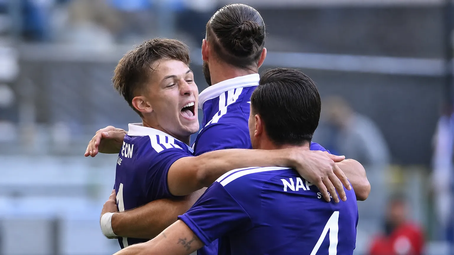 Drie Anderlecht-spelers vieren samen op het veld in paarse wedstrijdshirts.