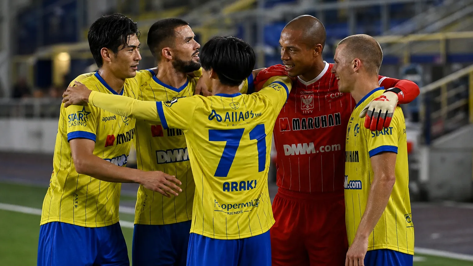 Een groep voetballers in gele wedstrijdkledij viert samen na een wedstrijd op Stayen.
