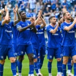 Een groep KAA Gent-spelers applaudisseert samen op het veld voor een tribune.