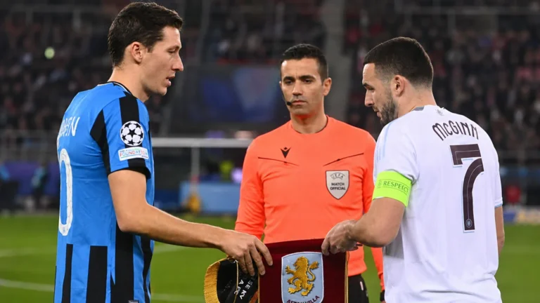 Een speler van Club Brugge en een speler van Aston Villa bij een Europese wedstrijd, met een scheidsrechter ertussen.