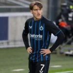Lynnt Audoor in een zwart tenue met blauwe strepen langs een voetbalveld.