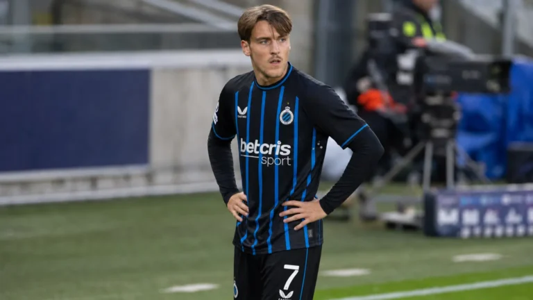 Lynnt Audoor in een zwart tenue met blauwe strepen langs een voetbalveld.