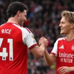 Twee Arsenal-spelers in rood-witte wedstrijdtenues vieren samen een moment op het veld.
