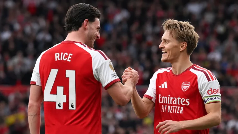 Twee Arsenal-spelers in rood-witte wedstrijdtenues vieren samen een moment op het veld.