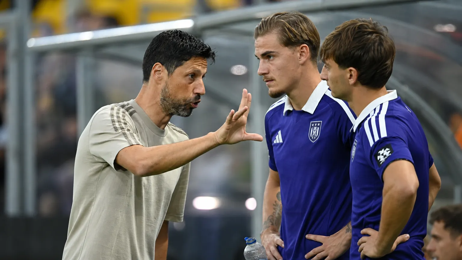 Een coach geeft aanwijzingen aan spelers in paarse shirts langs de zijlijn.