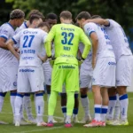 Een compacte groep KAA Gent-spelers overlegt in een huddle op het trainingsveld.