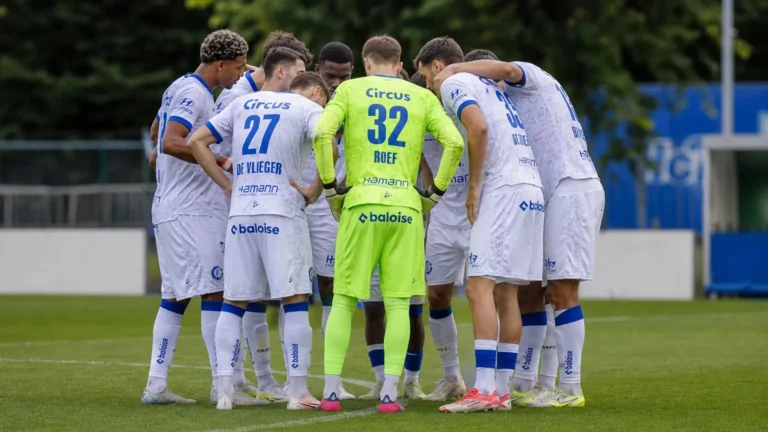 Een compacte groep KAA Gent-spelers overlegt in een huddle op het trainingsveld.