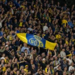 Een groep Union-supporters viert samen op een volle thuistribune met een Union-vlag.