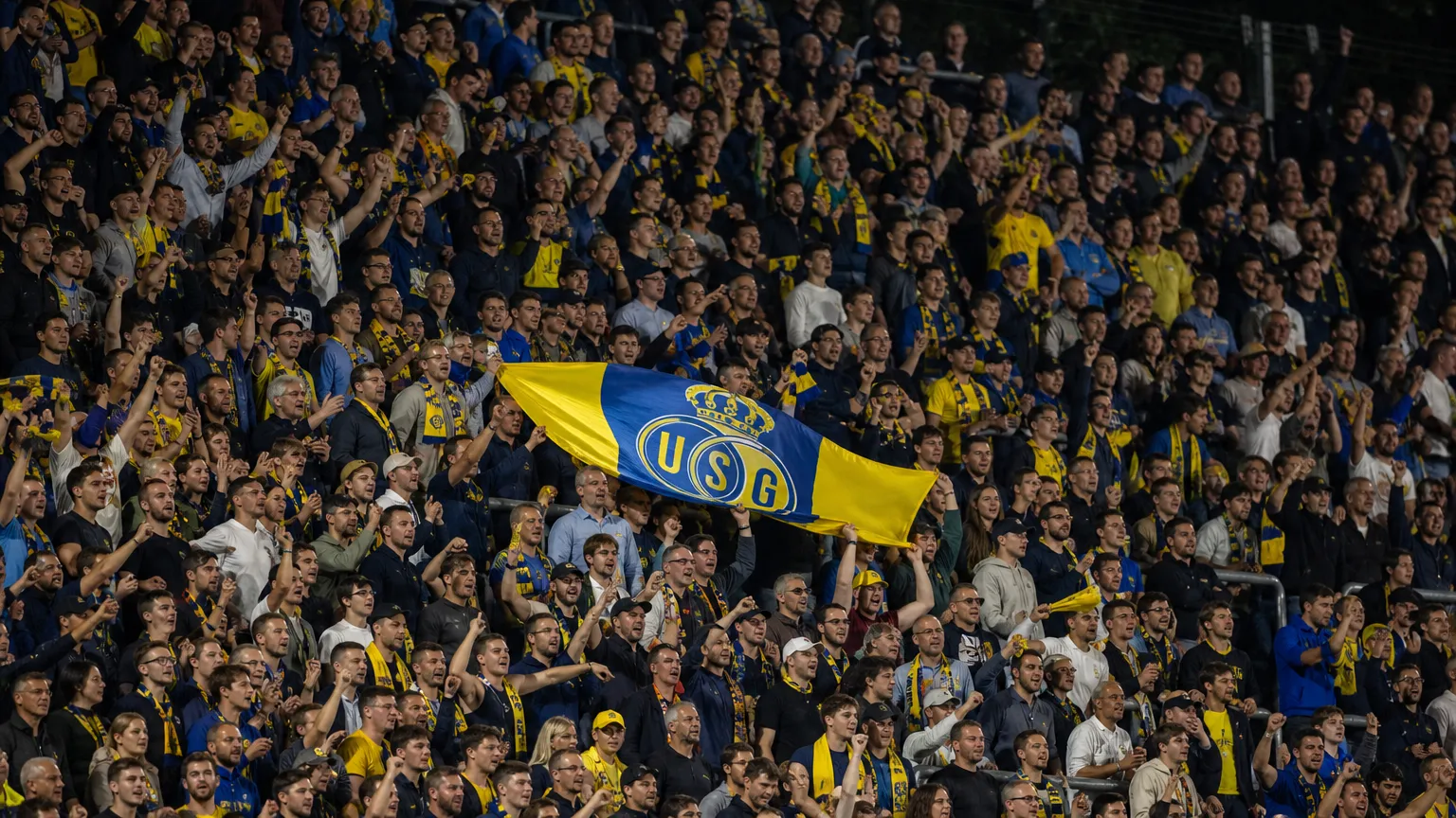 Een groep Union-supporters viert samen op een volle thuistribune met een Union-vlag.