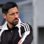 Vitor Bruno volgt aandachtig het spel vanaf de zijlijn in een zwart-witte sportjas.