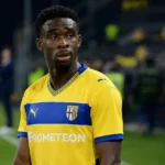 Mandela Keita in geel-blauwe spelerskleding langs de zijlijn van een voetbalveld.