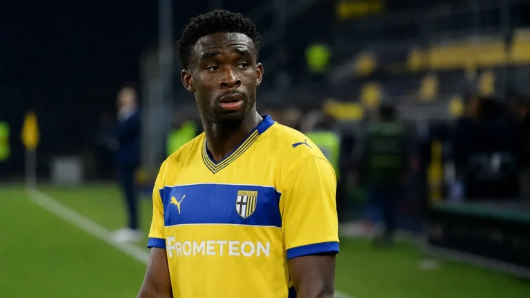 Mandela Keita in geel-blauwe spelerskleding langs de zijlijn van een voetbalveld.